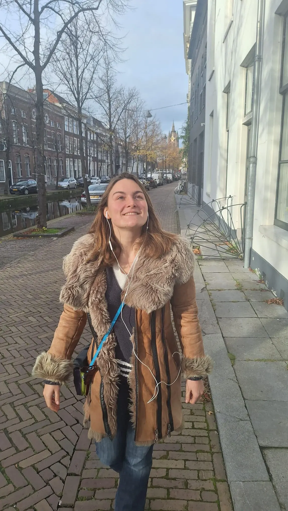 A woman walking beside a Delft canal wearing earphones, listening to the self-guided audio tour of Delft