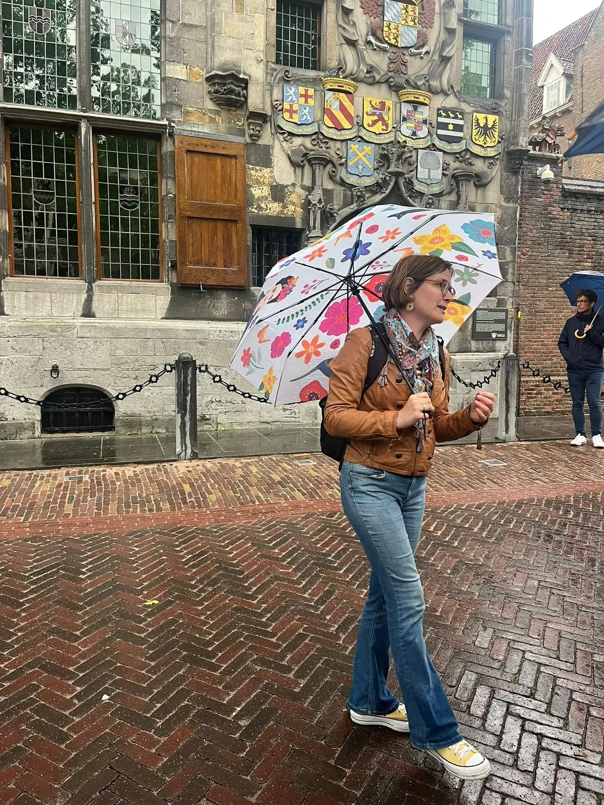 A guide passing the heraldic shields on the Gemeenlandshuis facade on a rainy Delft walking tour