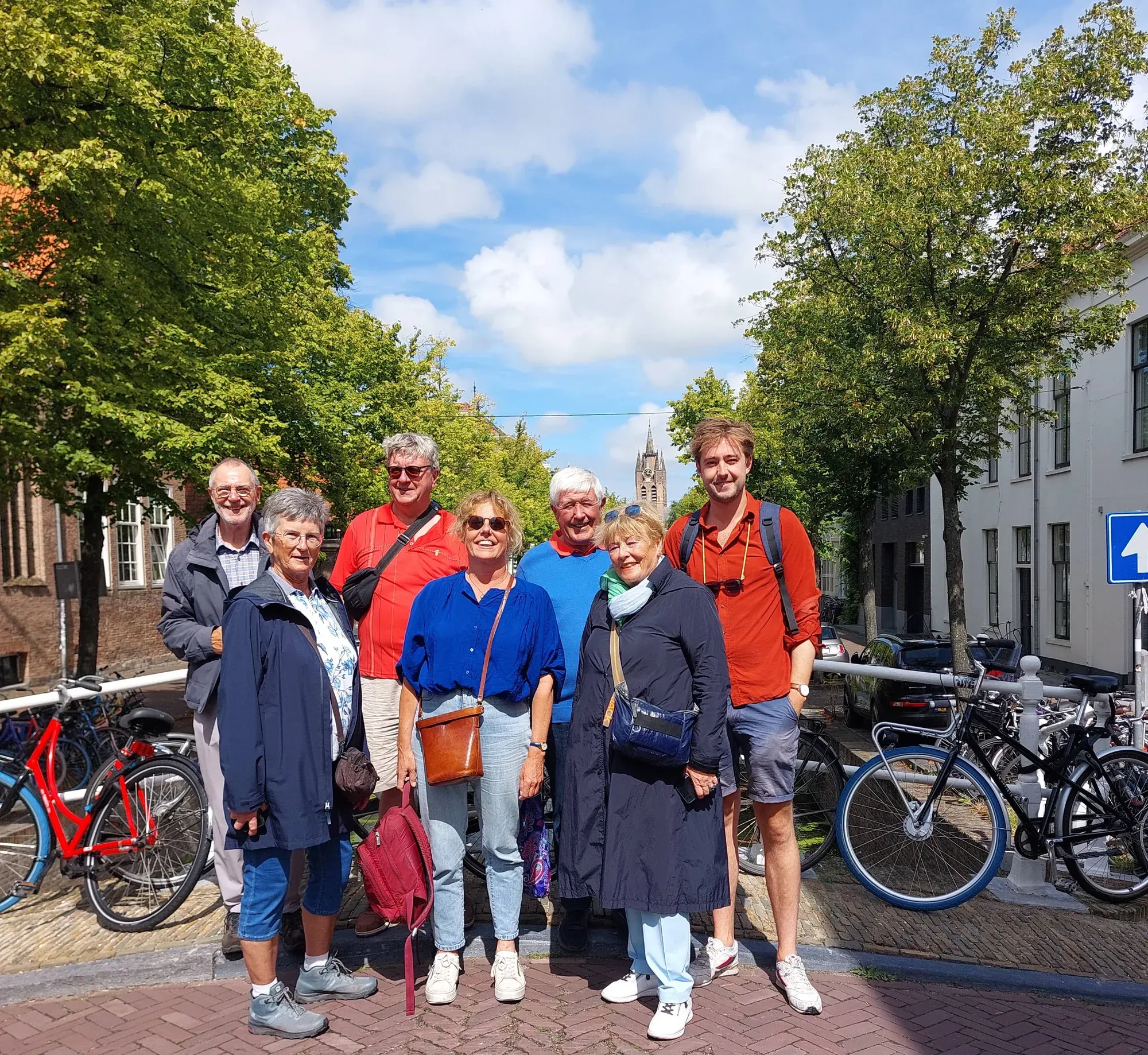 A tour group on a tree-lined canal bridge in Delft during a guided walking lunch between courses