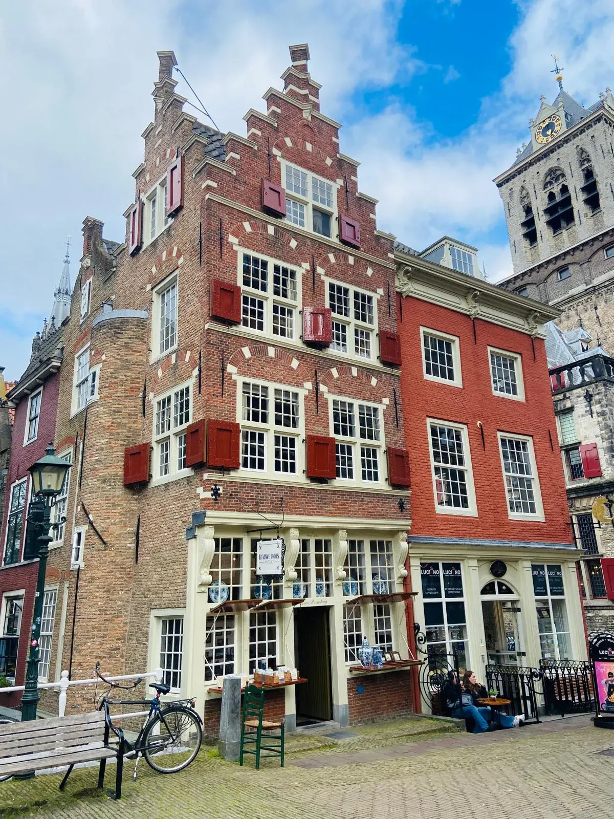A corner house with a Delftware shop sign and the Nieuwe Kerk tower behind it, Delft