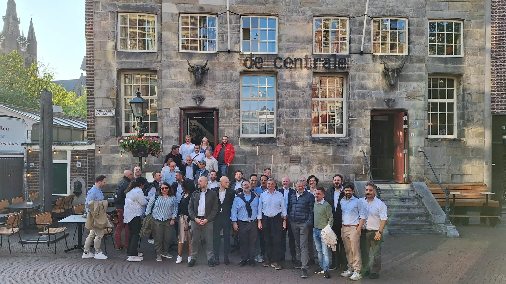 A large team building group posing together outside De Centrale restaurant in Delft, with the Nieuwe Kerk tower in the background