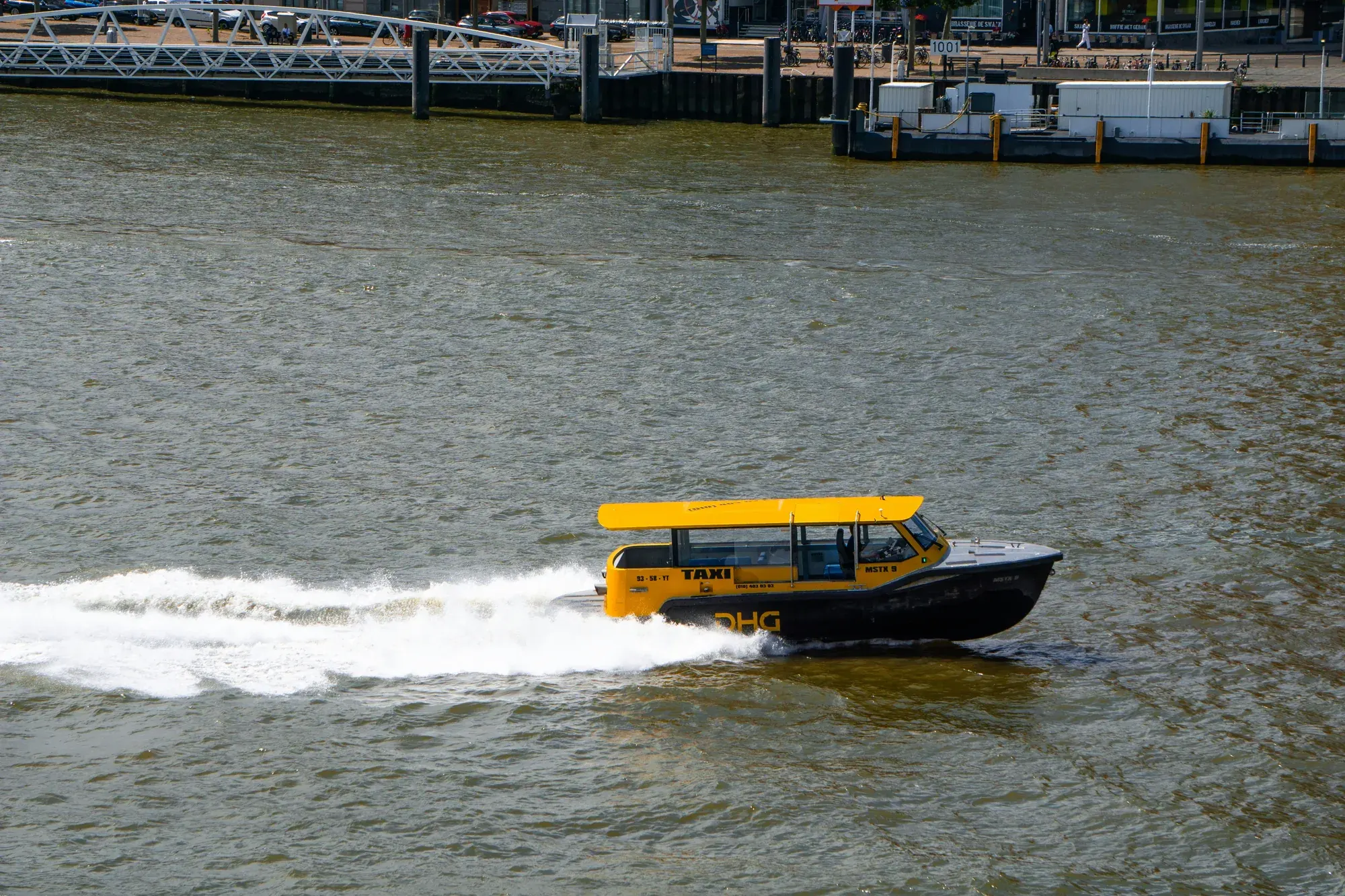 A yellow Rotterdam water taxi crossing the Nieuwe Maas at speed, part of the full-day Delft and Rotterdam private tour